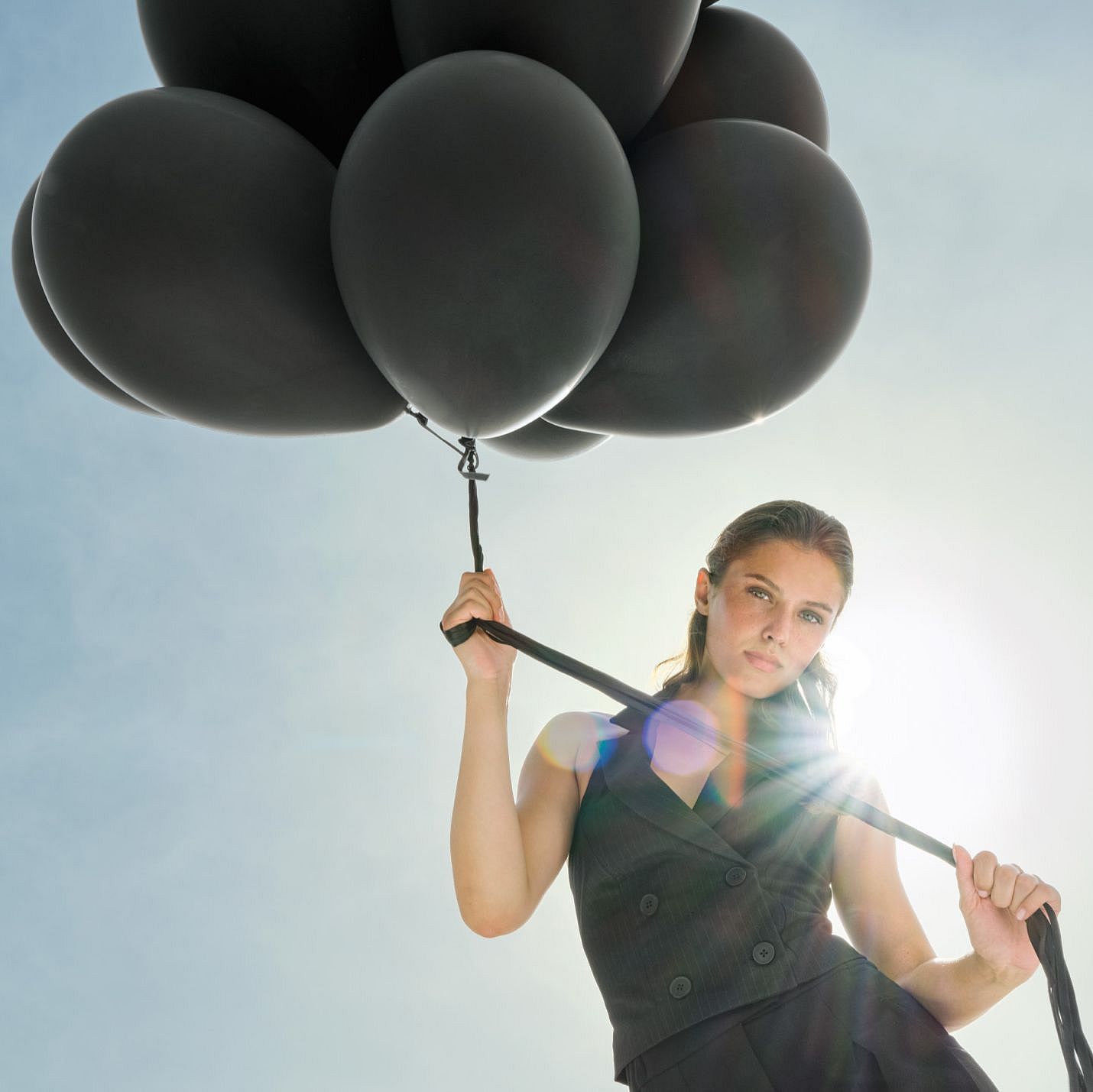 Una donna vestita di nero tiene dei palloncini neri fissati a dei nastri che fluttuano sopra di lei.