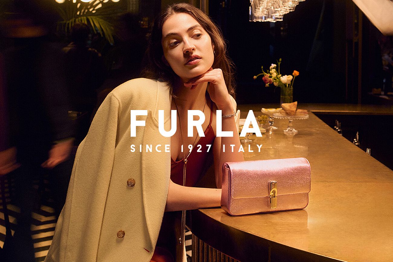 Una donna seduta al bar con una borsa Furla davanti a sé.