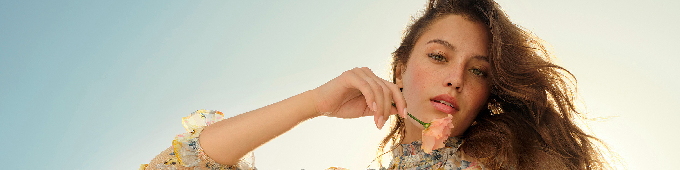 Viene mostrata la testa di una donna che tiene un fiore davanti al viso senza coprirlo.