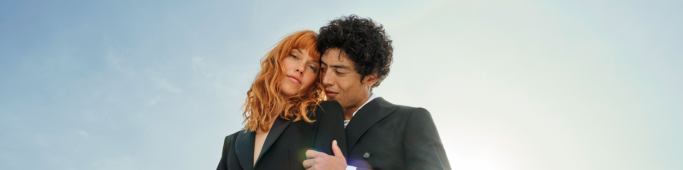 Una donna è in piedi e guarda nella telecamera mentre un uomo la tiene abbracciata da dietro.